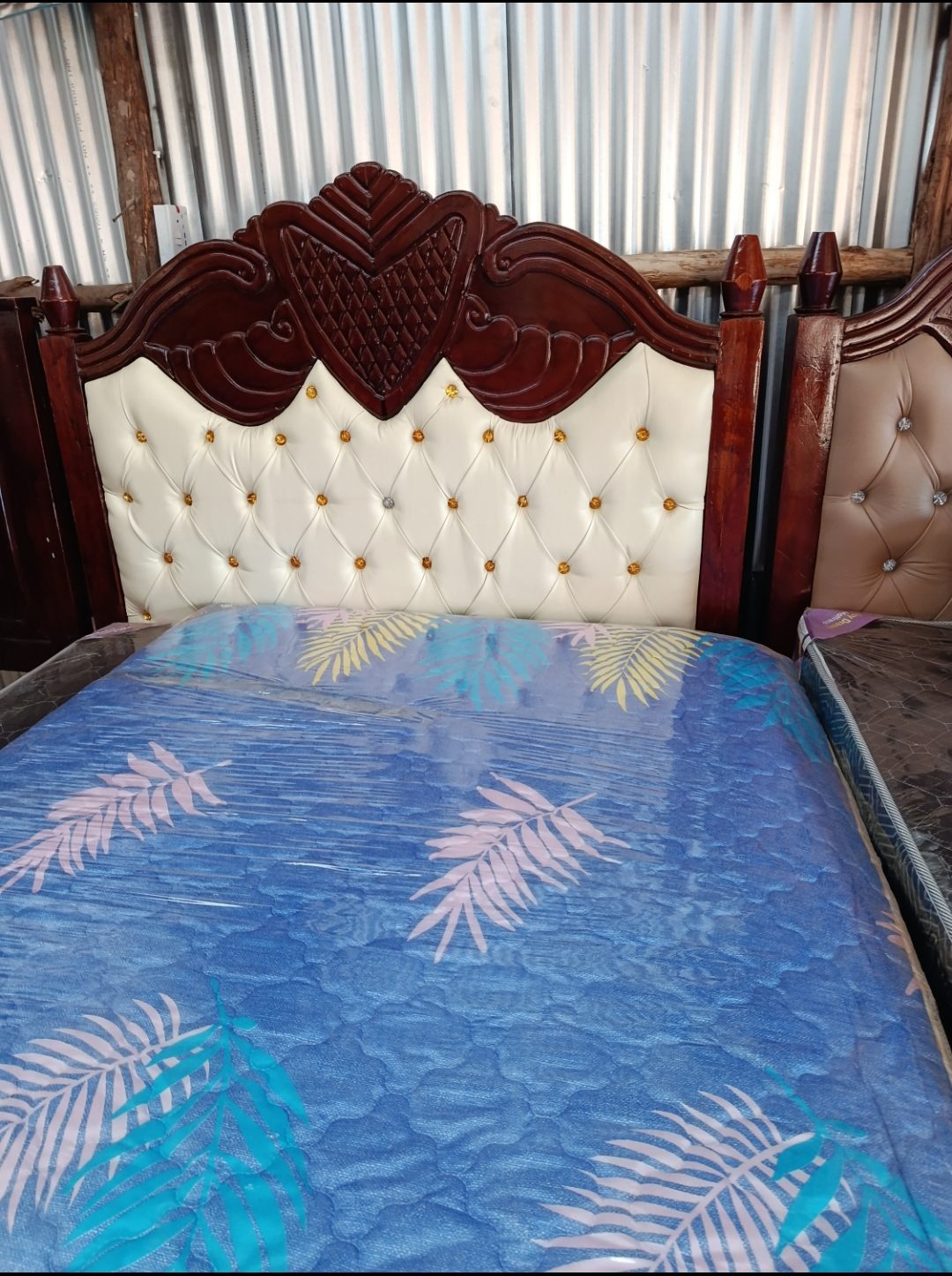 Carved mahogany bed with a cream tufted headboard and a mattress